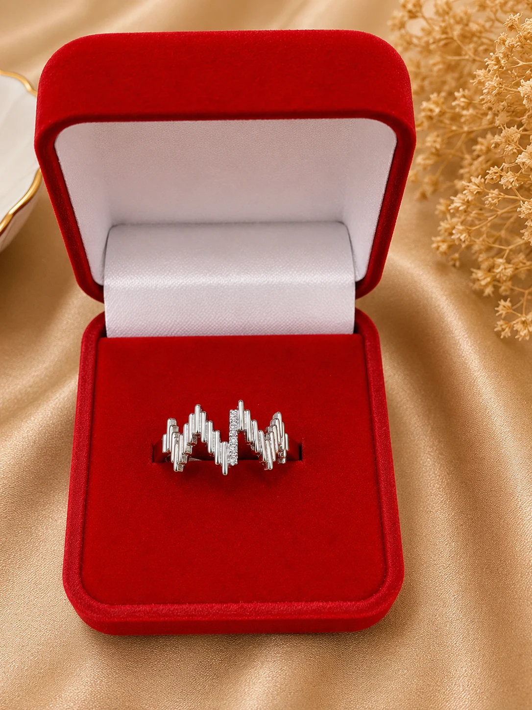 Silver Crystal Lightning Wave Ring (1) Elegant silver star-shaped ring with sparkling stone detailing, photographed on champagne-beige satin
