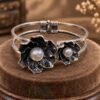 featuring two sculpted flowers, engraved petals, luminous pearl-style centres and a hinged double band.